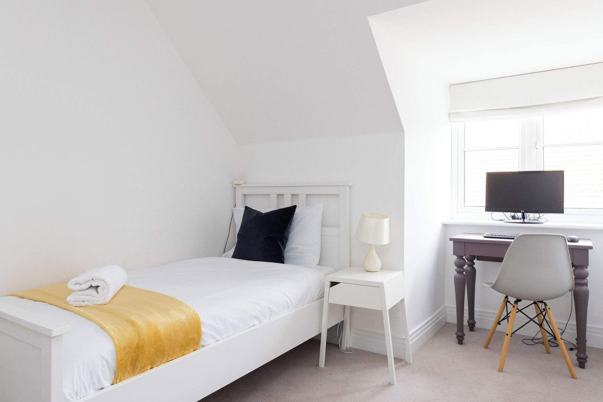 A bedroom with a bed, a desk, a chair, and a window.