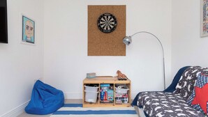 A room with a dartboard, a desk with storage, a bean bag, and a bed with patterned bedding. - Modern Family Retreat Nr Beaches and Marina (Birdham)