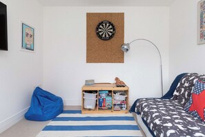 Ein Zimmer mit Dartscheibe, einem Schreibtisch mit Stauraum, einem Sitzsack und einem Bett mit gemusterten Betttextilien.