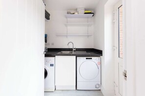A compact laundry room with a washing machine, dryer, sink, and a small shelf above the sink.