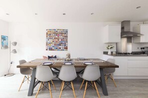 Eine moderne Küche mit weißen Schränken, einer Edelstahl-Dunstesse und einem Essbereich mit Holztisch und grauen Stühlen.