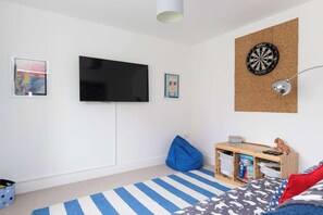 Ein Zimmer mit Flachbildfernseher, Dartscheibe, Sitzsack, kleinem Holztisch mit Stauraum und einem Streifenmuster-Teppich.
