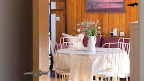 A dining area with a wooden wall, a table with chairs, a vase with flowers, and a painting above the table.