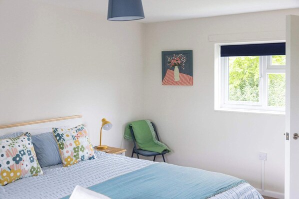 A bedroom with a bed, a chair, a lamp, a window, and a painting on the wall.
