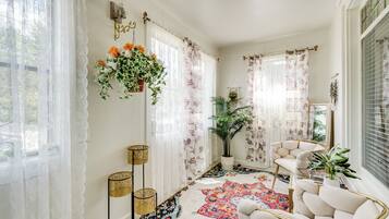 Een gezellige kamer met een kamerbreed tapijt, een hangplant en een witte fauteuil.