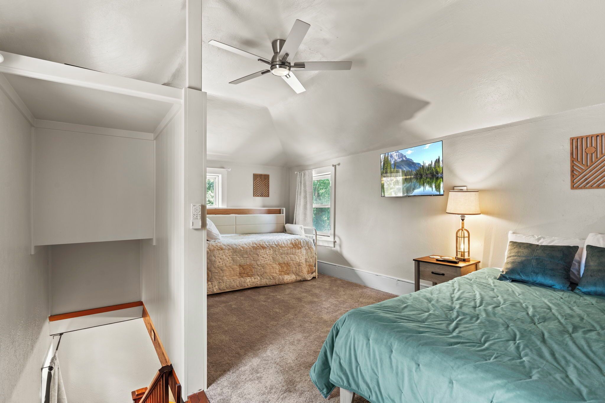 Une chambre à coucher avec un lit, un ventilateur de plafond, une table de chevet avec une lampe, une fenêtre donnant sur les montagnes et un téléviseur fixé au mur.