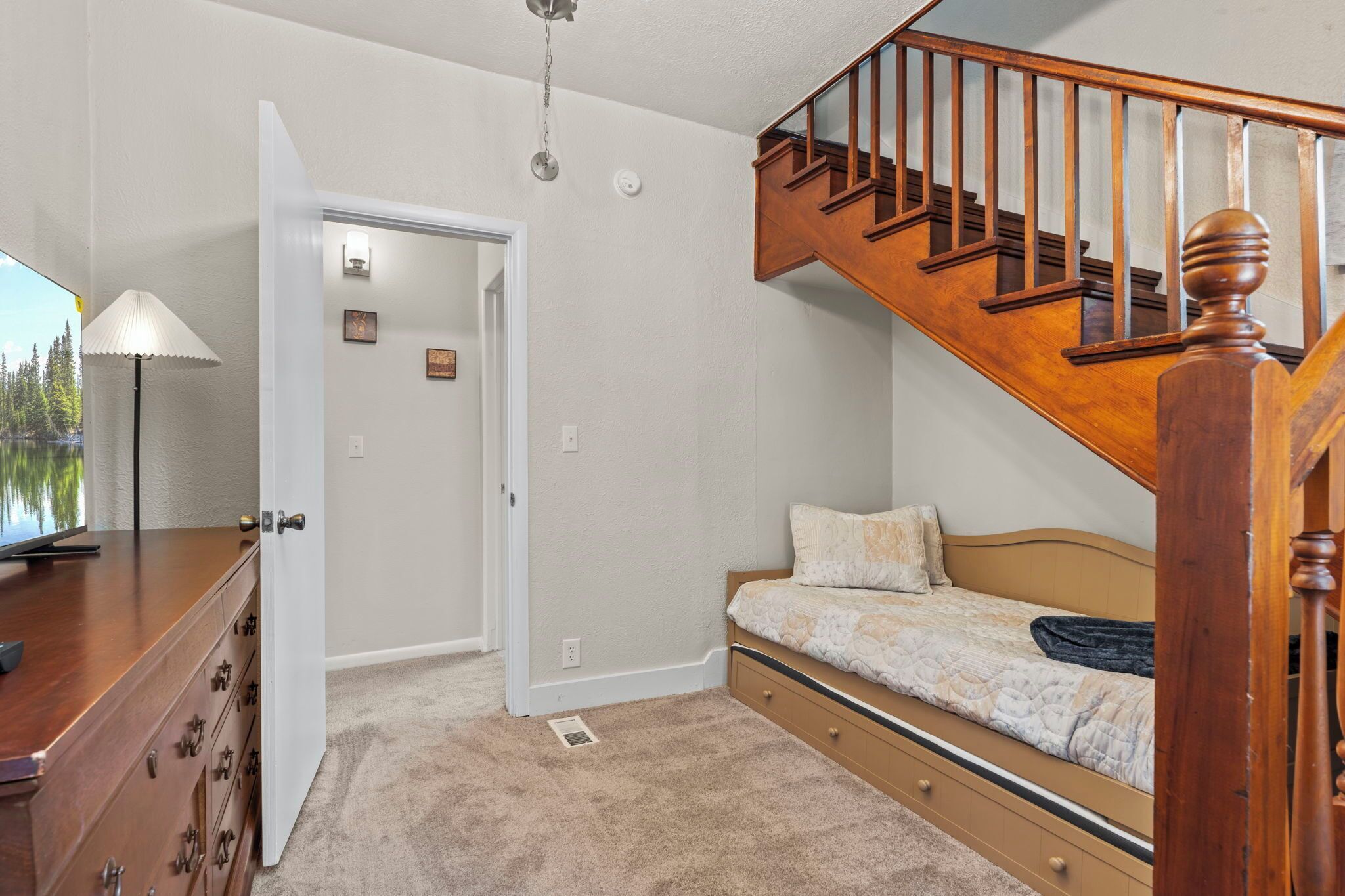 A bedroom with a wooden bed, a nightstand, a lamp, and a staircase.