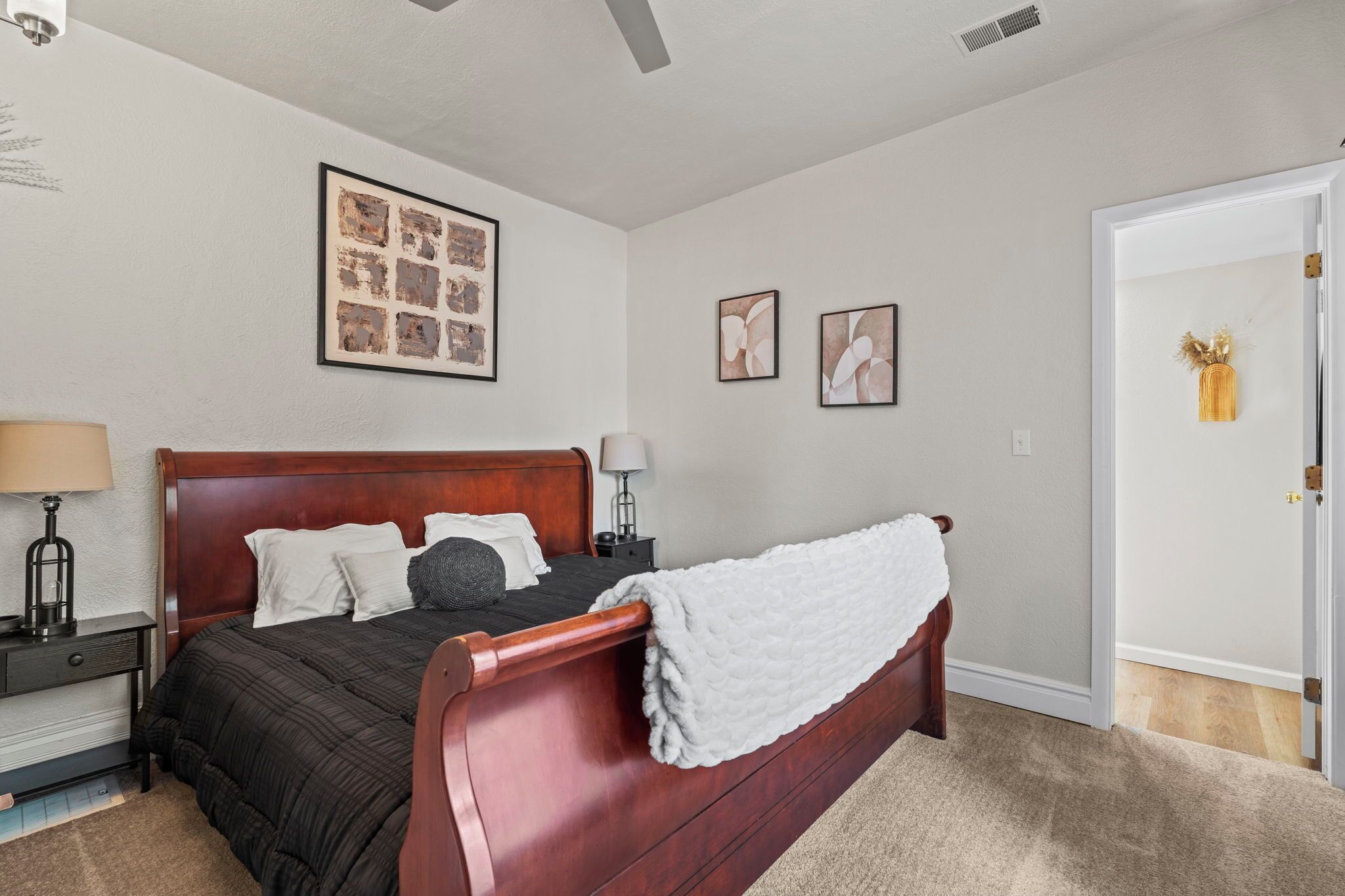 A bedroom with a wooden bed, a nightstand, a lamp, and framed artwork on the wall.