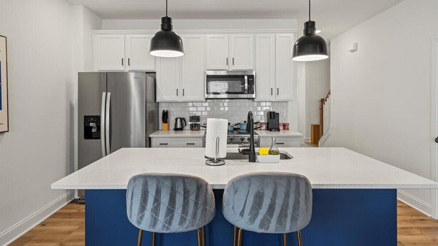 A modern kitchen with white cabinets, stainless steel appliances, a central island with bar stools, and pendant lighting. - 3BR Townhouse Mins to Uptown Charlotte (Charlotte)