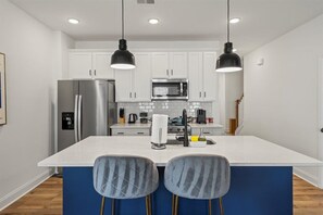 A modern kitchen with white cabinets, stainless steel appliances, a central island with bar stools, and pendant lighting. - 3BR Townhouse Mins to Uptown Charlotte (Charlotte)