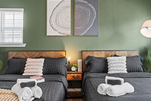 Ein Hotelzimmer mit zwei Betten, dunkler Bettwäsche und einem Nachttisch mit Lampe und Büchern.