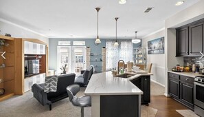 Cocina moderna con isla de mármol, armarios negros e iluminación colgante.