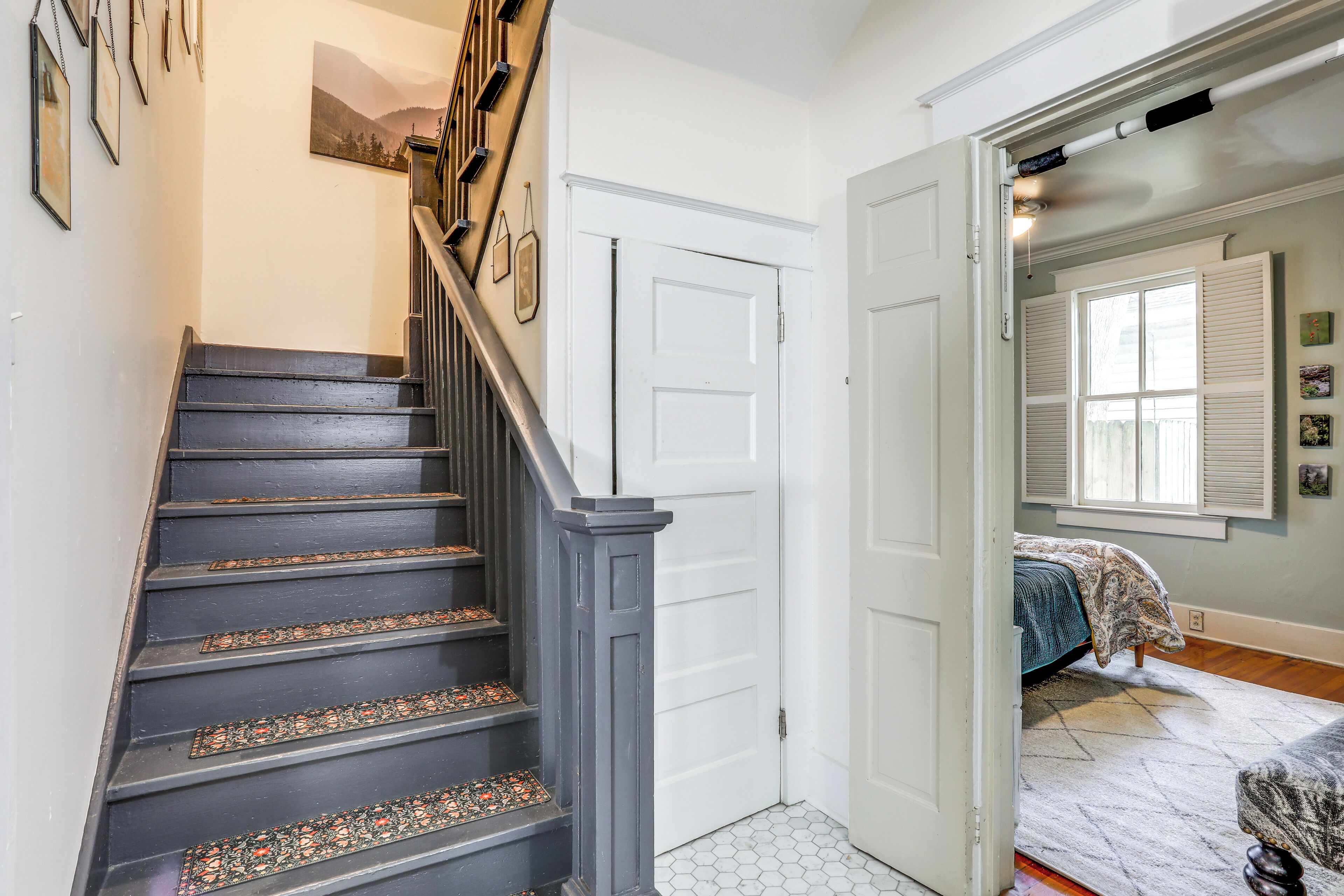 Una escalera con barandillas decorativas, una puerta blanca y un dormitorio con cama y ventana.