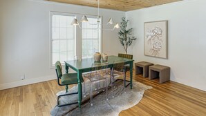 A dining area with a wooden ceiling, a glass table, clear chairs, and a light fixture. - From the Square to Ole Miss: Historic Oxford Home (Oxford)