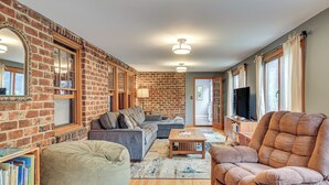 A living room with a brick wall, a sofa, a bean bag, a coffee table, and a television. - Easy Train Access to NYC! Elegant Family Retreat (West Orange)