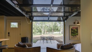 A room with a glass ceiling, wicker furniture, a framed poster, and a view of an outdoor area with trees. - Unique Studio on Obanyon Creek in Dtwn Loveland! (Loveland)
