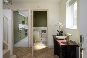 A modern kitchen with green cabinets and a wooden herringbone floor.