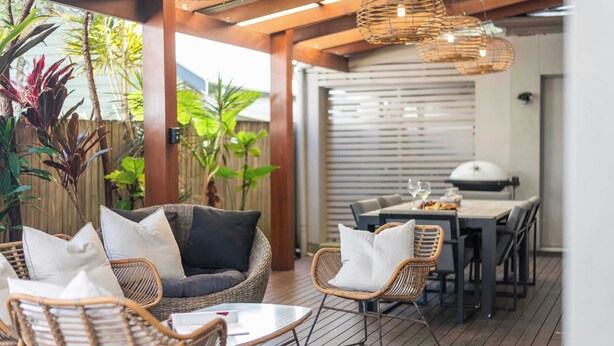 An outdoor patio with wicker furniture, a dining table, and a grill area.