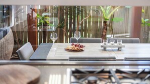 An outdoor dining area with a table set for four, surrounded by chairs, and a view of greenery through a bamboo fence.