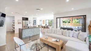 A modern living room with a sofa, coffee table, and chairs, a kitchen with a bar, and a dining area with a table and chairs.