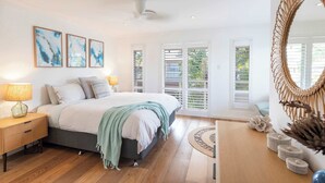 A bedroom with a bed, bedside tables, a mirror, and a view through the window.