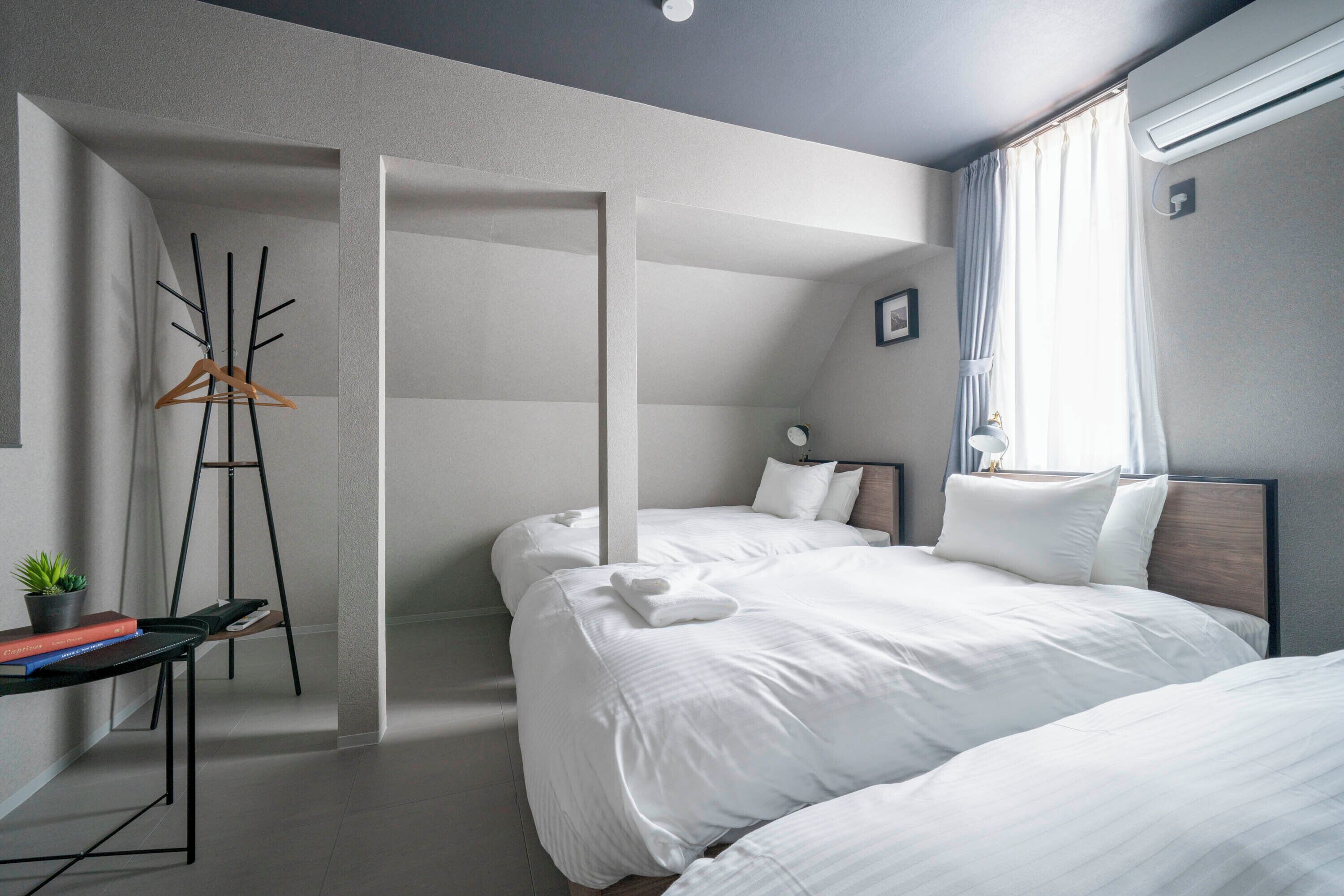 A modern hotel room with two beds, a desk with a plant, and a coat rack.