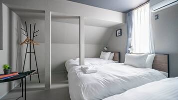 A modern hotel room with two beds, a desk with a plant, and a coat rack.