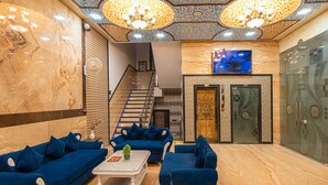 A lobby with blue sofas, a white coffee table, and a staircase leading to upper floors.