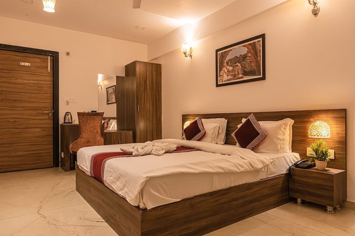 Una cama bien hecha con tablero de madera, una lámpara de noche y una mesita de noche con un teléfono y una planta.