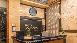 A hotel reception desk with a clock, a sign for 'Hotel Jodhaina Palace', and a reception area.