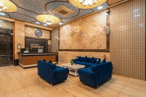 A hotel reception area with a reception desk, a clock, and seating with blue sofas.