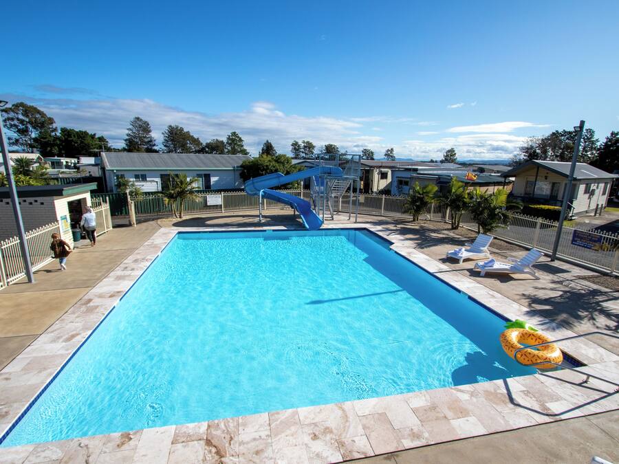 A rectangular swimming pool with a blue slide, surrounded by lounge chairs and a small inflatable float.