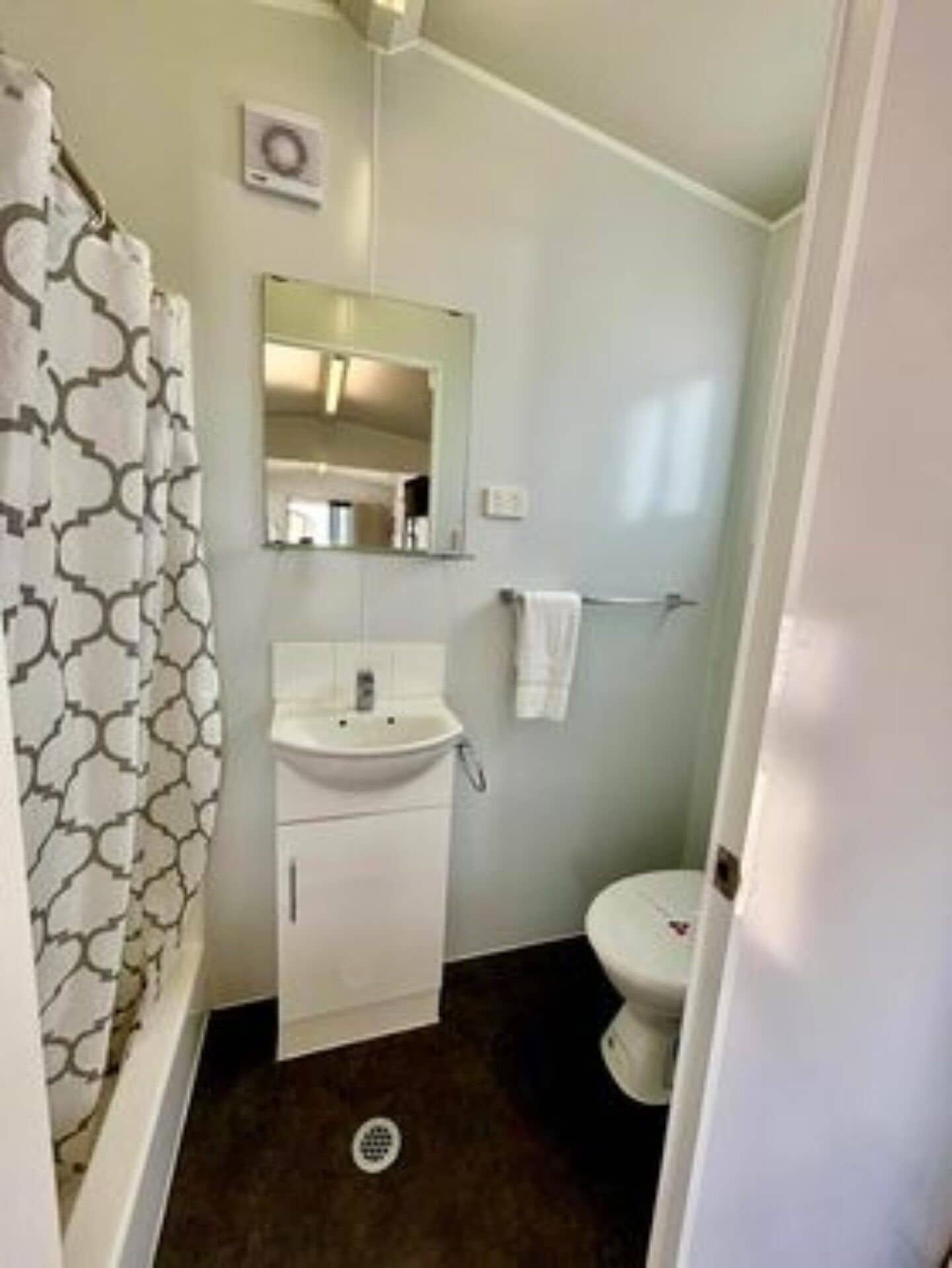 A bathroom with a white sink, a mirror above it, a toilet, and a shower curtain with a geometric pattern.