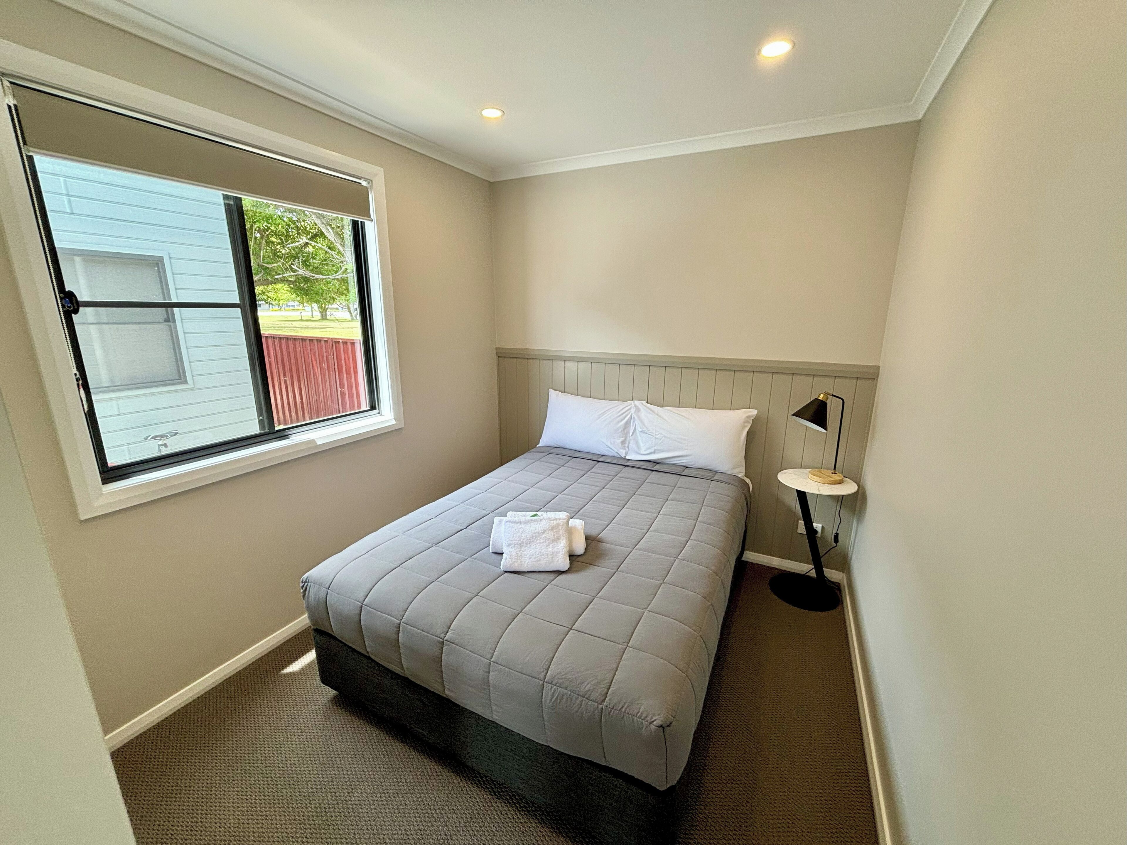 A bedroom with a bed, a window, a nightstand, and a lamp.