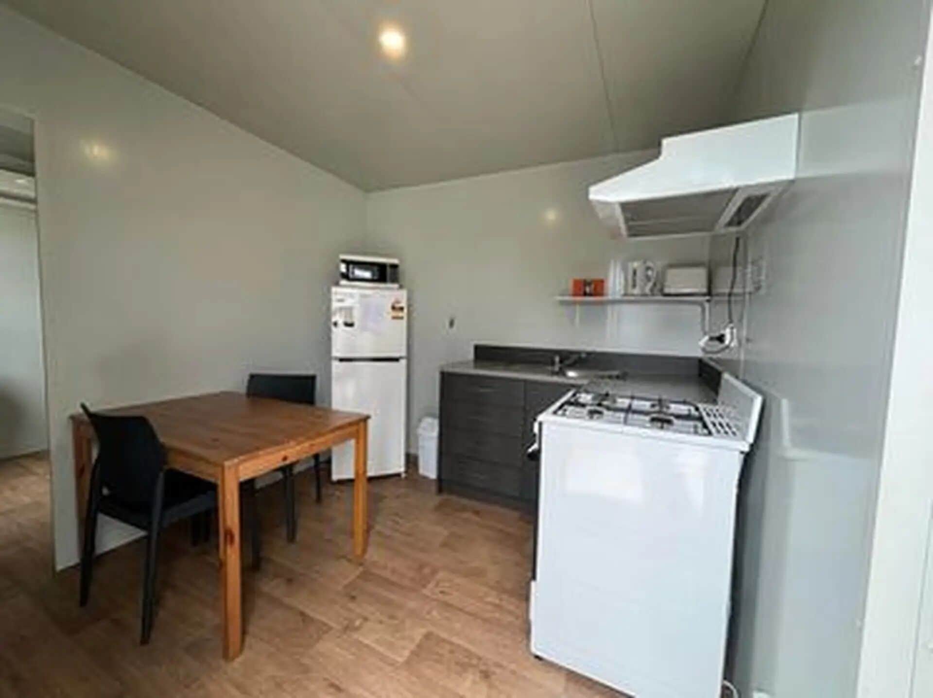 Cocina compacta con estufa a gas, microondas y refrigerador. Una mesa de madera con dos sillas.