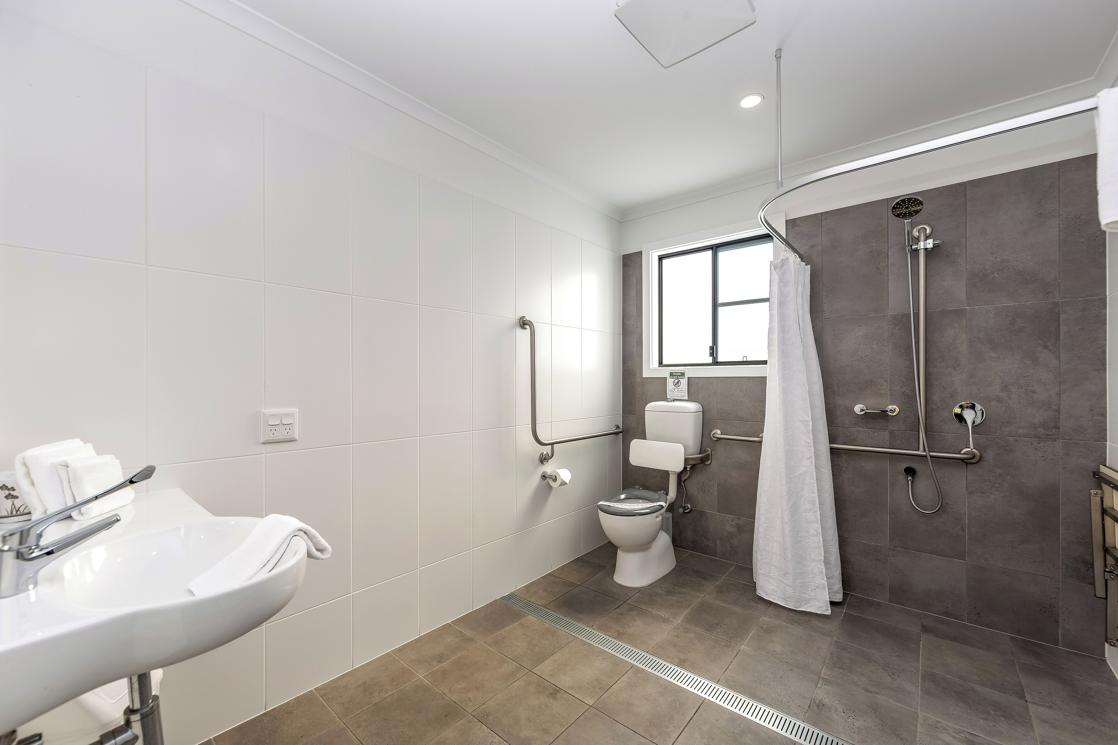 Ein modernes Badezimmer mit Waschbecken, Toilette und Duschbereich in Weiß.