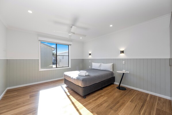 Un dormitorio con cama, ventilador de techo, ventana y una pequeña mesa.