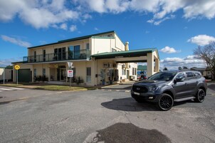 Un edificio de dos pisos con techo verde, un letrero de restaurante chino y un estacionamiento con un SUV Ford.