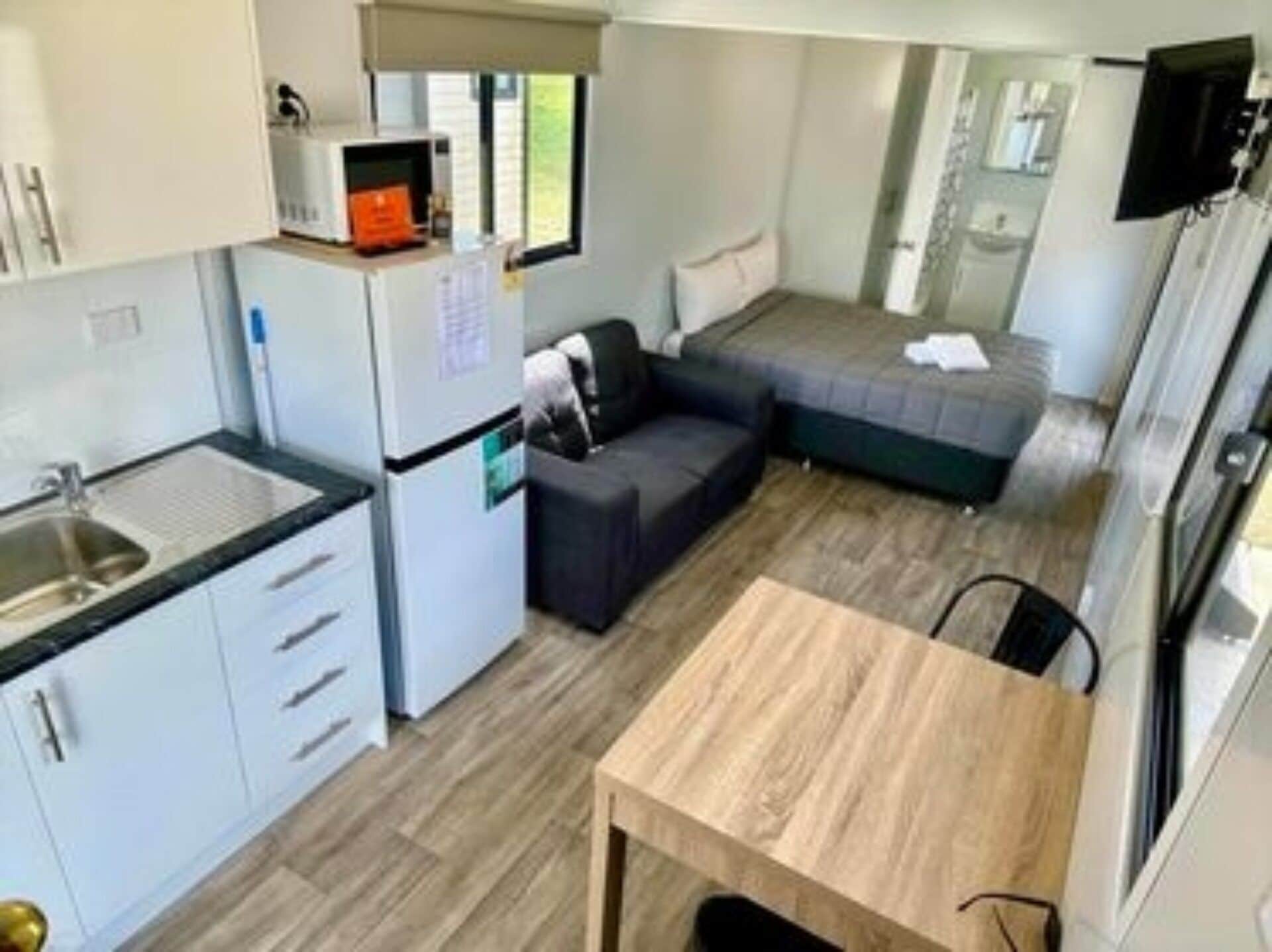 A compact kitchen with a sink, cabinets, and a microwave. There is a small dining table and a sofa in the living area.