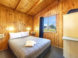 Una habitación con paneles de madera, una cama, dos lámparas de noche, una ventana y un refrigerador.