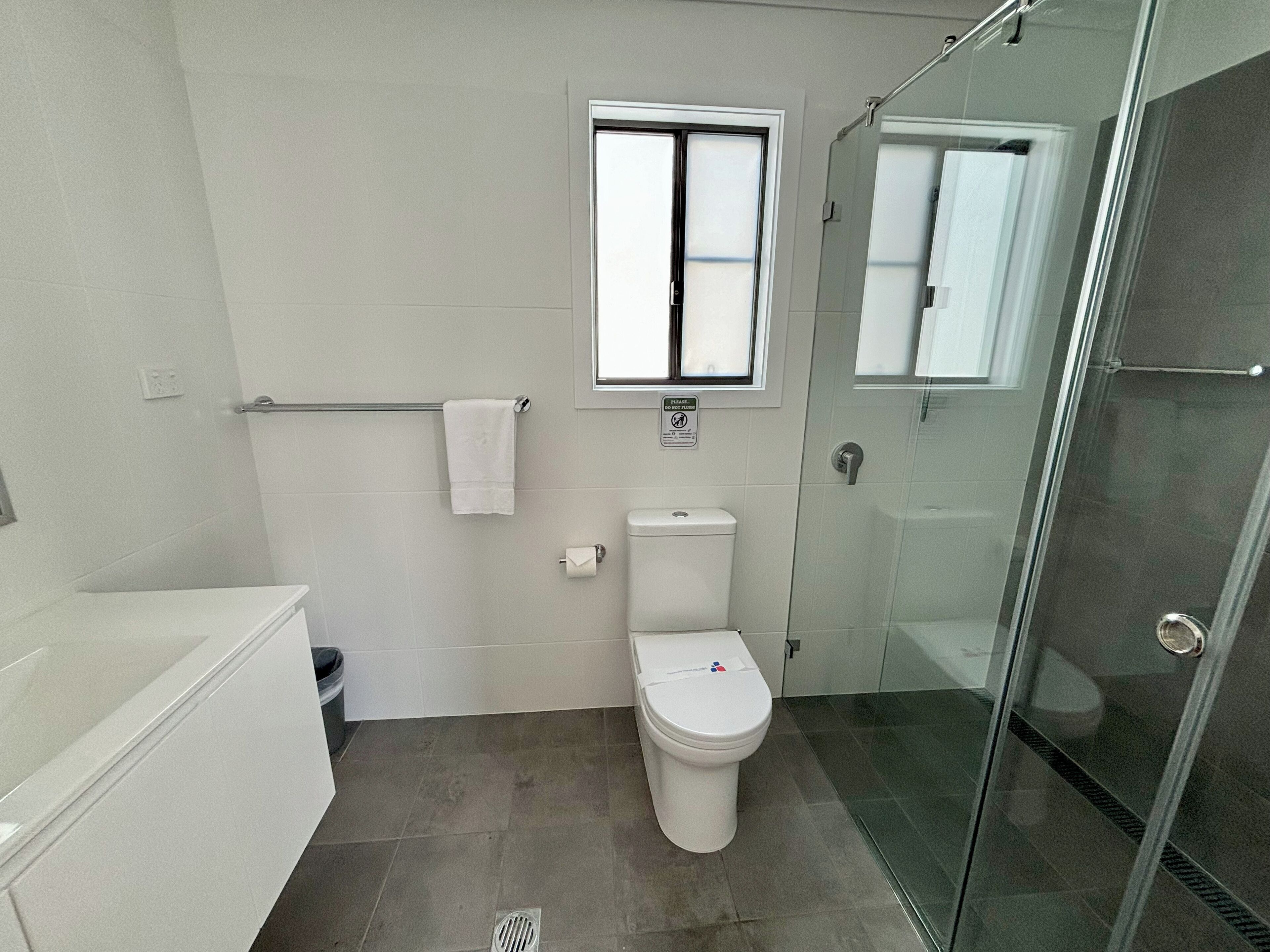 Un baño moderno con inodoro, cabina de ducha de vidrio, ventana y toallero.