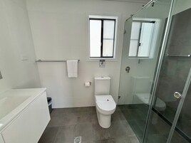 Un baño moderno con inodoro, cabina de ducha de vidrio, ventana y toallero.