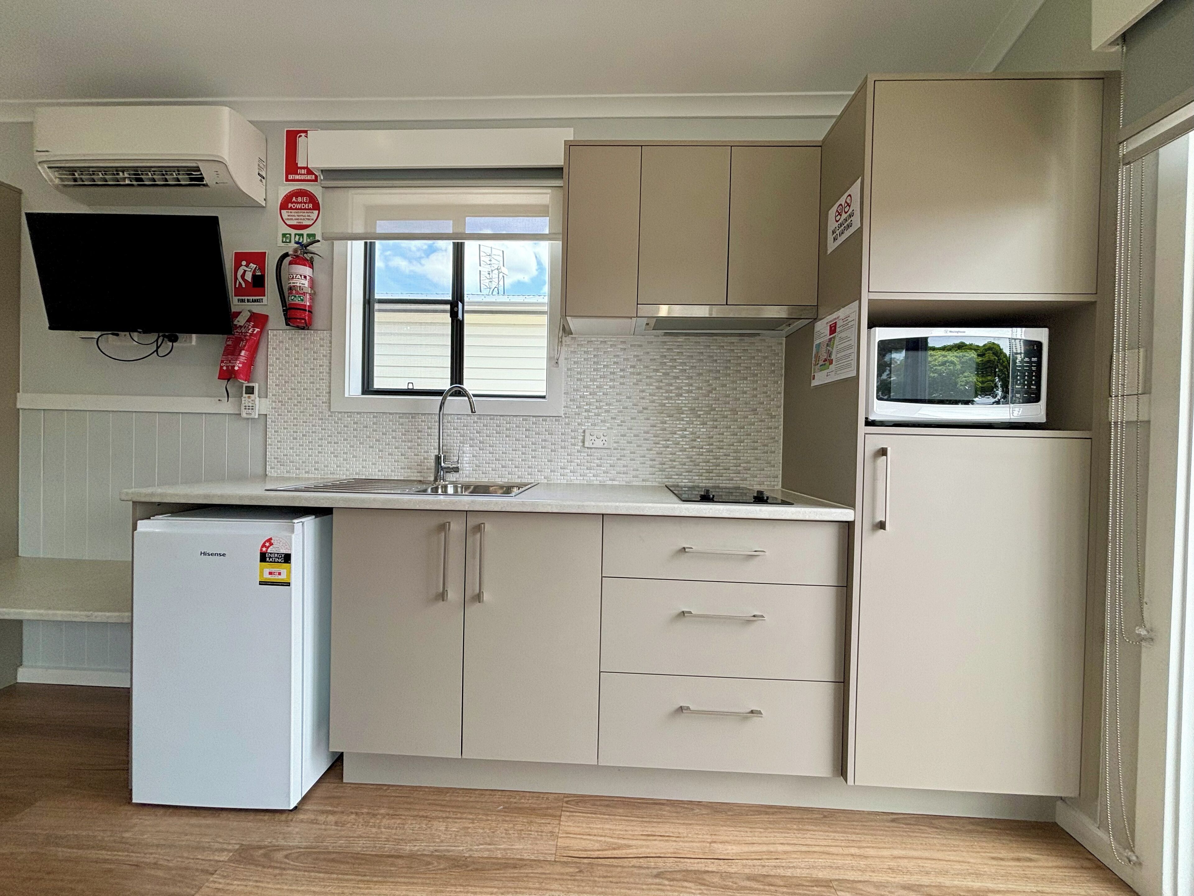 A compact kitchen with a refrigerator, microwave, and a window with blinds.