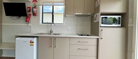 A compact kitchen with a refrigerator, microwave, and a window with blinds.