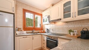 Une cuisine avec des meubles blancs, un four à micro-ondes, une cuisinière et une fenêtre donnant sur un paysage verdoyant.