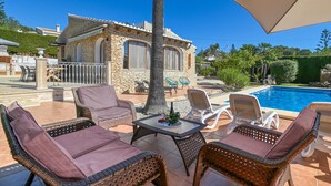 Una villa de piedra con piscina, mobiliario de mimbre y una pérgola.