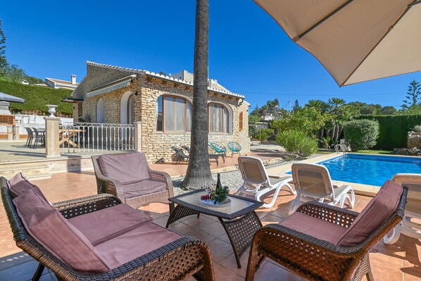 Une villa en pierre avec une piscine, des meubles en osier et une pergola.