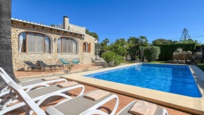 A poolside area with lounge chairs, a stone building, and a clear blue sky. - Casa Montana 4 pax - Javea, Costa Blanca (Javea)