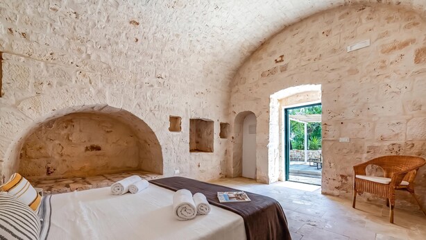 A room with a bed, a chair, and a view through an open doorway. - Lamia Terra 3br, Terrace & BBQ (Castellana Grotte)