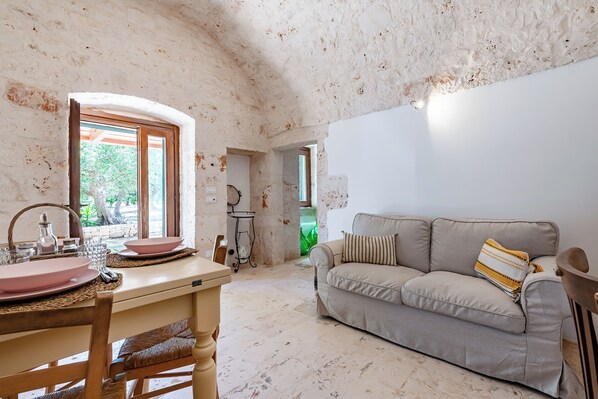 Una habitación con mesa de comedor, sillas, sofá y una zona de cocina.